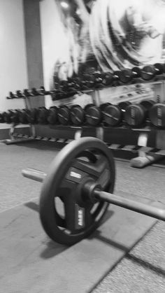 a black and white photo of a gym with rows of dumbbells in the background