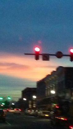 a traffic light hanging over a city street at night with the sun setting in the background