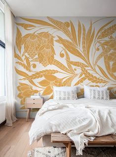 a bed sitting under a window next to a wall with flowers painted on the side