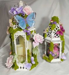 two white lanterns with flowers and butterflies on them, one has a candle in it