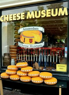 there are many cheeses on display in the store front window and behind it is a sign that says cheese museum