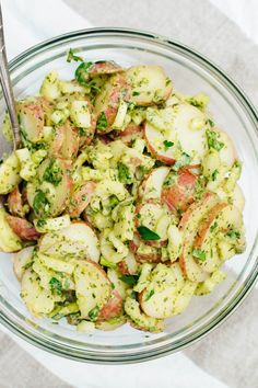 a glass bowl filled with potato salad on top of a white table cloth next to a fork