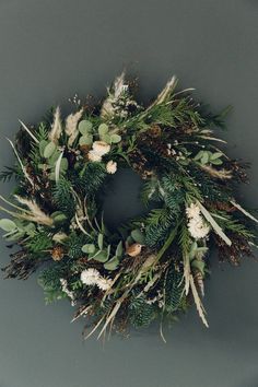 a wreath with green leaves and white flowers on a gray background, hanging from the wall