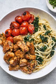 a white bowl filled with pasta, chicken and cherry tomatoes on top of a table