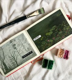 an open book sitting on top of a bed next to two paintbrushes and some other items