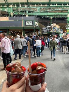 a person holding up two cups with ice cream and strawberries in them on the street