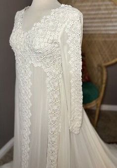 a white wedding dress with long sleeves and lace on the top, in front of a chair