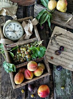 an assortment of fruit is displayed in wooden boxes on a table with music sheets and clock