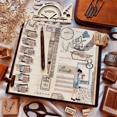 an open notebook with stamps, scissors and other things on it next to a pair of scissors