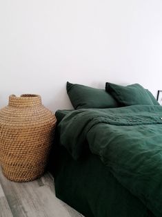 a bed with green sheets and pillows next to a basket on the floor in front of it