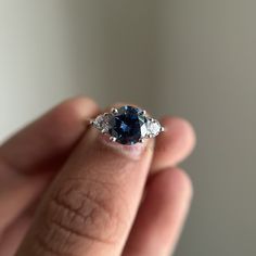 a woman's hand holding an engagement ring with a blue sapphire and three diamonds