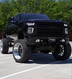 a black truck with big tires parked in a parking lot