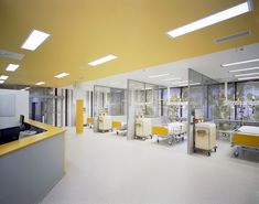 an empty hospital room with yellow and white beds in the middle, and lights above them