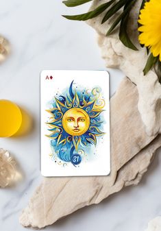 the sun tarot card is next to some yellow flowers and glasses on a marble surface