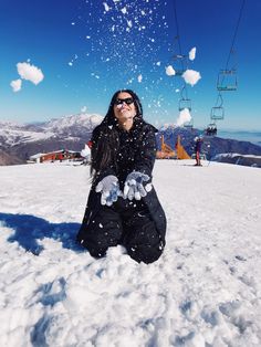 a woman sitting in the snow on top of a ski slope throwing snow into the air