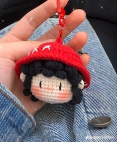 a hand holding a tiny crocheted doll wearing a red hat and blue jeans