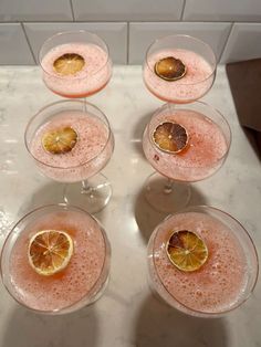 four glasses filled with pink liquid and lemons on top of a marble countertop