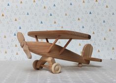 a wooden toy airplane sitting on top of a white table next to a wall with triangles