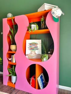 an orange and pink book shelf with plants on it