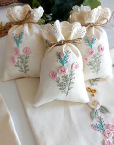 three embroidered bags with flowers on them sitting on a table next to a basket full of flowers