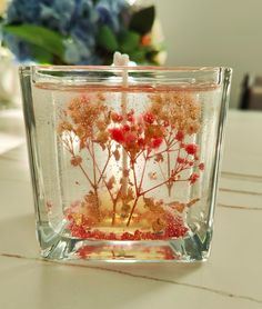 a vase filled with water and flowers on top of a white table next to a blue flower arrangement