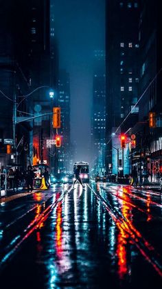 a city street at night with cars and traffic lights reflecting off the wet road surface