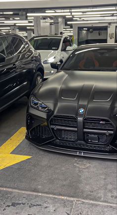 several cars parked in a parking garage with yellow arrow painted on the floor and one black car