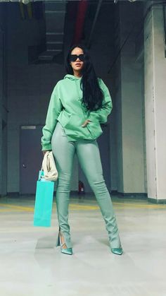 a woman in green is holding a blue bag and posing for the camera with her hands on her hips