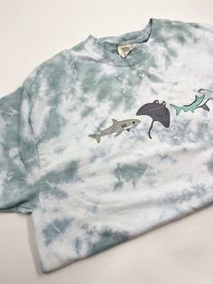 The perfect summer t-shirt for hanging out at the beach! Beautiful hand dyed sage/ocean blue tie dye that is super unique to each t-shirt! These are Comfort Colors brand and are unisex! If you have any concerns for sizing we always recommend to size up because we’d rather it be a touch big than too small! We do suggest to wash all items in cold water and dry on low heat to prevent shrinkage and fading of the tie dye. If you need your item by any particular date please email or message us before Beach Tshirt Ideas, Shark Tshirts, Ocean Shirt, T Shirt Prints, Oversized Shirts, Shark Shirt, Shark T Shirt, Beach T Shirts, Beach Beautiful