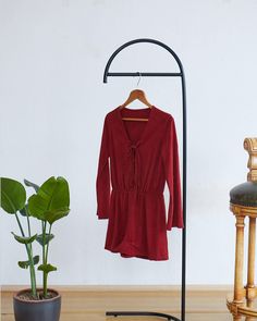 a red shirt hanging on a clothes rack next to a potted plant and chair