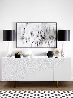 a white cabinet with black lamps and a painting on the wall above it in a living room