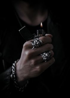 a person holding a lighter in their hand and wearing rings with skulls on the ring