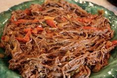 a green plate topped with shredded meat and veggies on top of a table