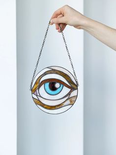 a hand holding a stained glass eye hanging from a chain, with the eye being held up