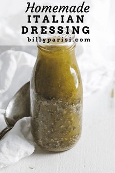 homemade italian dressing in a glass jar on a white tablecloth with a spoon next to it