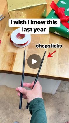 someone is holding two chopsticks in their hand and they have wrapped presents on the table