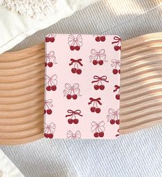 a pink notebook with cherries and bows on it sitting on top of a wooden table