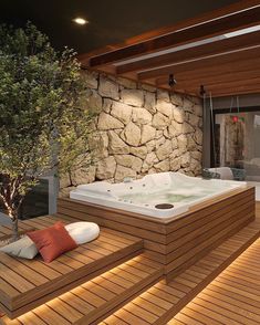 a large hot tub sitting on top of a wooden deck next to a stone wall