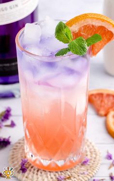 an orange and purple drink sitting on top of a table next to grapefruits