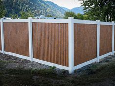 a white fence with brown slats on it in front of some trees and mountains