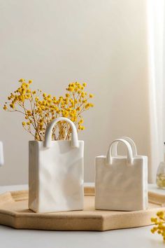 two white bags sitting on top of a wooden tray next to yellow wildflowers