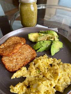 a plate with eggs, toast and avocado next to a jar of pickles