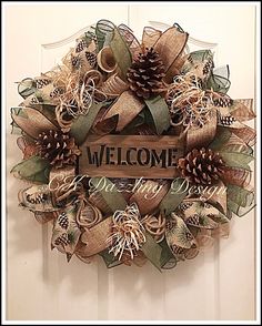 a welcome wreath with pine cones and ribbons hanging on a door handle that says welcome