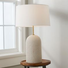 a white lamp sitting on top of a wooden table next to a window in a room