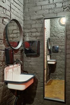 a bathroom with brick walls and mirror, sink and hair dryer on the wall