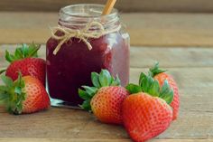 strawberries and jam in a jar on a wooden table with two strawberries next to it