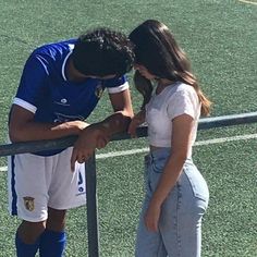 a man and woman standing next to each other near a fence on a soccer field