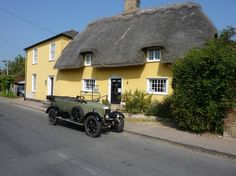 an old car is parked in front of a yellow house with a thatched roof