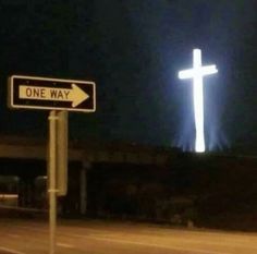 a one way street sign in front of a large cross on a hill at night