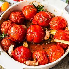 roasted tomatoes and onions in a white casserole dish with herbs on the side